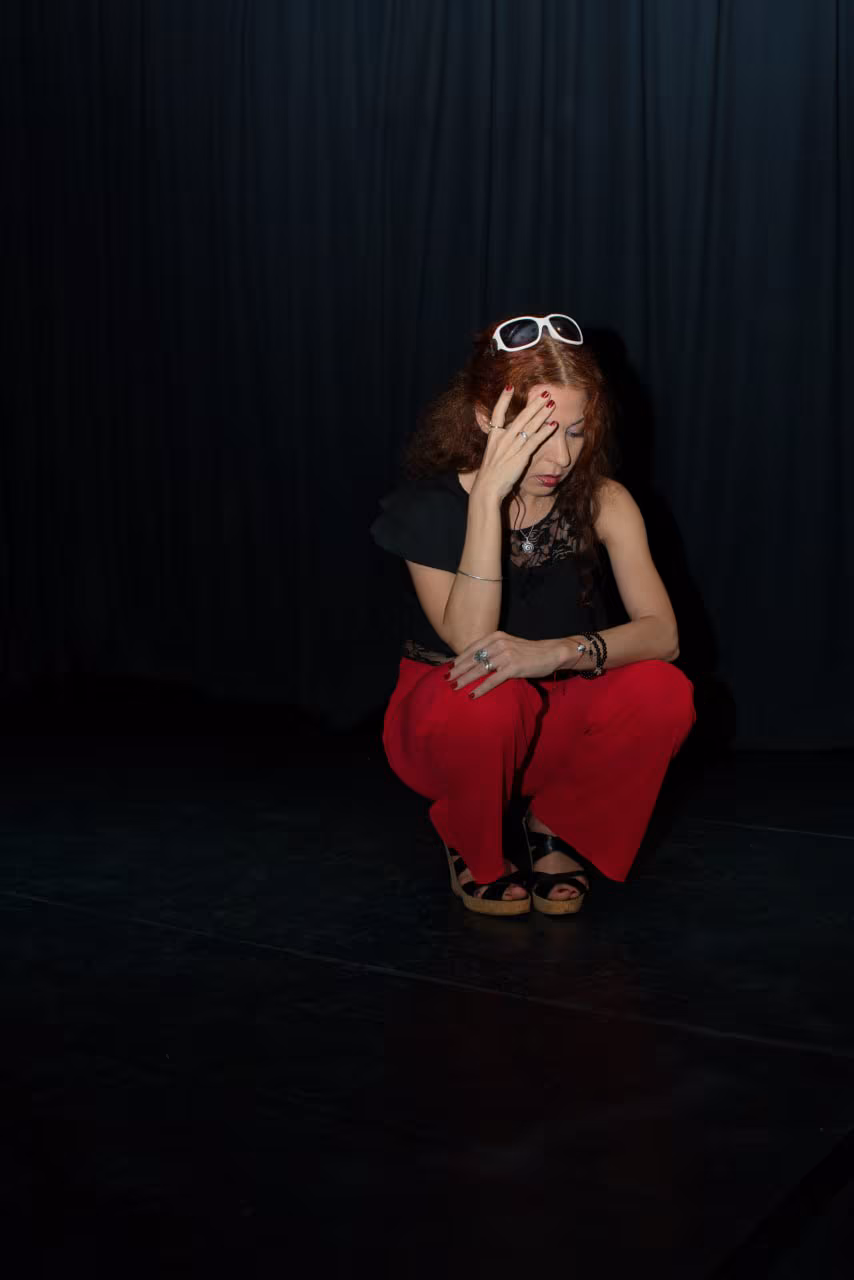 Eva ArtVision agachada en escena, vestida de negro y rojo, entre bambalinas