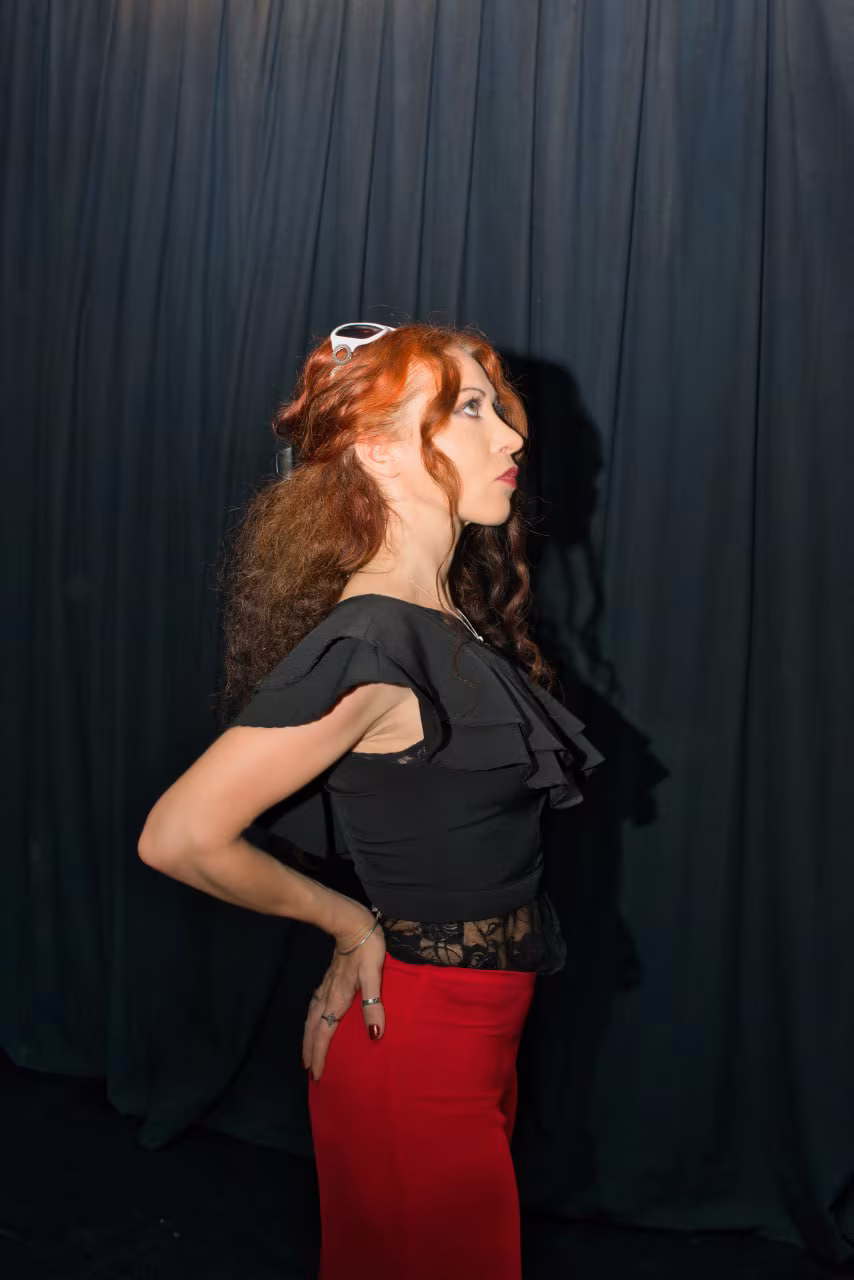 Eva ArtVision de perfil entre bambalinas de teatro, vestida de negro y rojo