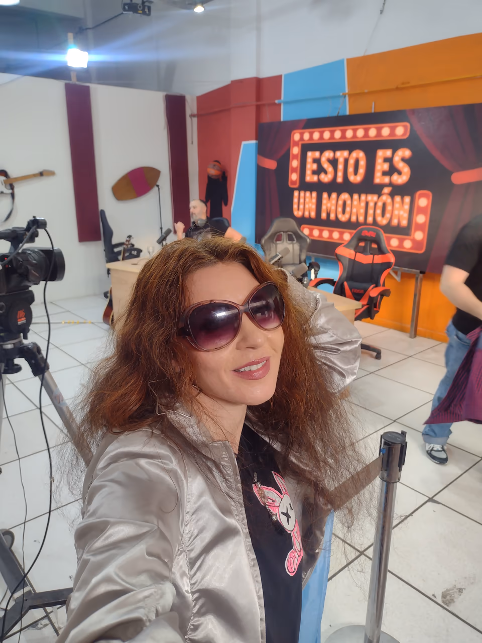 Eva ArtVision en un set de TV con cámaras y el cartel «Esto es un montón» de fondo, retrato tipo selfie