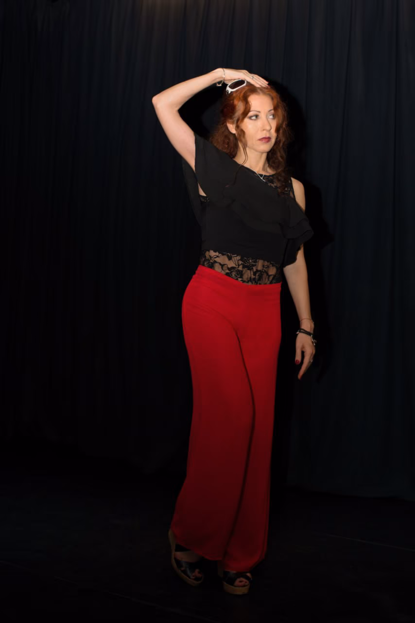Eva ArtVision de cuerpo entero en escena, pantalón rojo y top de encaje negro, con el brazo sobre la cabeza